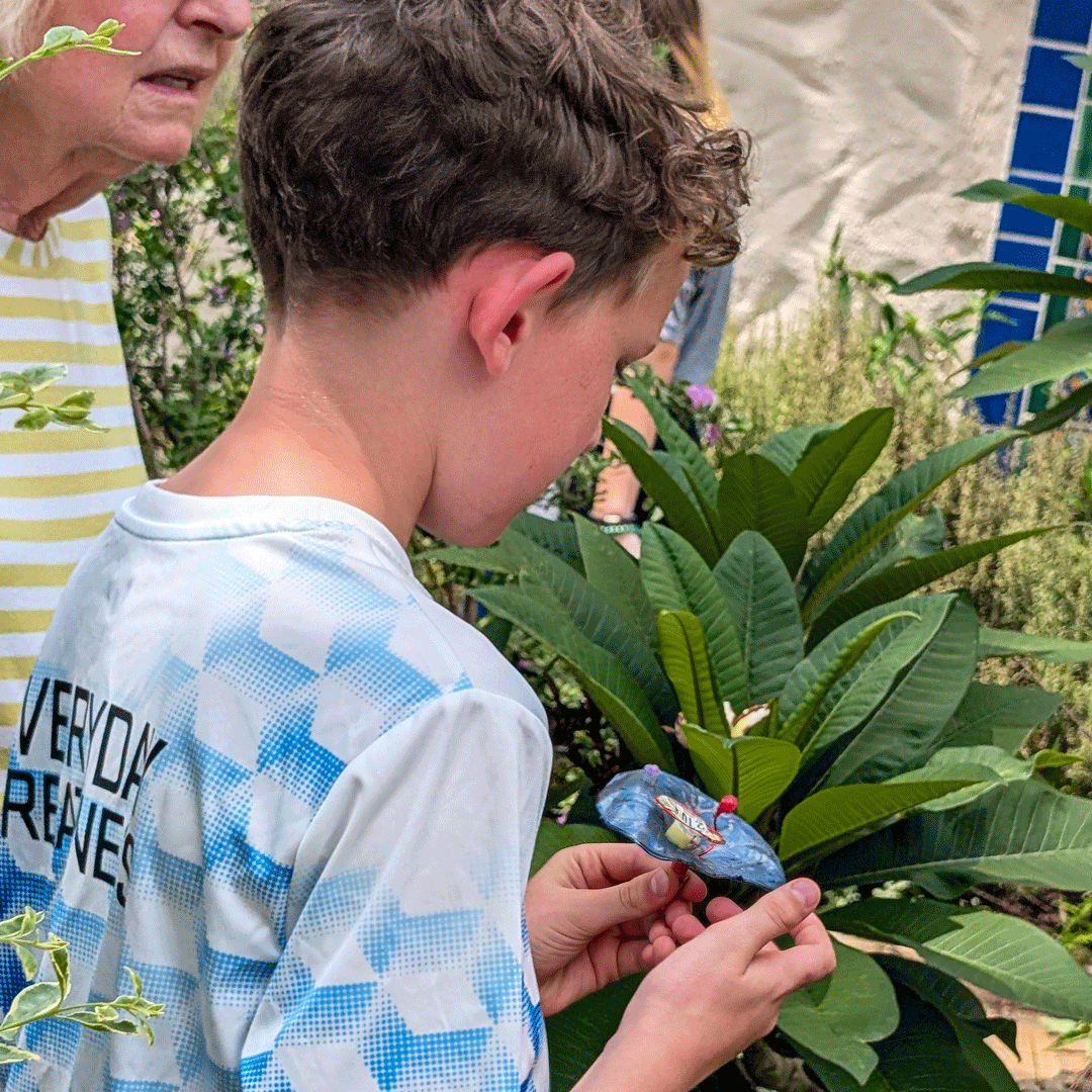 A young participant examines one of Margaret Craig's Setting Seed sculptures after finding it among the plants on Blackburn Patio at the McNay Art Museum.
